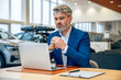 © zinkevych - Businessman sitting in dealership office working on automobile contract processing car sale