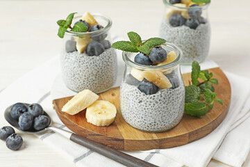 Wall Mural - delicious chia pudding with blueberries, banana and mint in glasses on light table, closeup