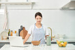 © Dialogue Frame - A young Asian woman cooks in the kitchen while checking her laptop