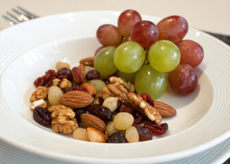 Poster -  Bowl with grapes and nuts on white surface. 