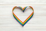 A vibrant rainbow ribbon forming a heart, a symbol of LGBTQ+ love and pride, on a rustic white wood background.