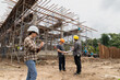 © skarie - Female Construction manager is inspecting work on a construction site with engineer and foremen working or consulting behind her.