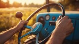 Farmer's hands on the steering wheel of an old blue tractor driving through a sunny field at sunset