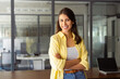 © Stock 4 You - Cheerful smiling latin hispanic female student standing hands crossed in office or university campus. Portrait beautiful young indian female specialist, business woman looking happy at camera at work