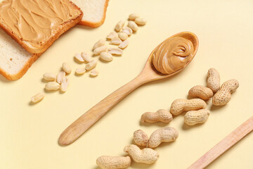 Wall Mural - wooden spoon with tasty peanut butter, toasts and nuts on beige background