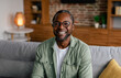 © Prostock-studio - Headshot of cheerful adult african american man in glasses and casual relaxing on sofa and looking at camera in living room interior, close up. Business and work at home during covid-19 quarantine