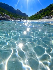 Poster - Crystal clear turquoise water with sunlight creating sparkles and caustic patterns on surface, mountains and green cliffs in background, split underwater view.