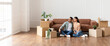 © Prostock-studio - Moving Day. Lovely couple sitting on the floor in new home with cardboard boxes around. Happy man and woman dreaming, looking aside at window, free copy space, panoramic banner for advertisement