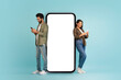 © Prostock-studio - Stylish beautiful young eastern couple posing by huge phone with white blank screen, cheerful handsome indian man and pretty long-haired woman using smartphones, colorful background, mockup