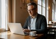 © Dina - Mature businessman concentrating on his laptop, enjoying a cup of coffee in a warm and inviting cafe atmosphere