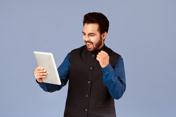 Poster - Excited Indian man with tablet computer making YES gesture on violet background