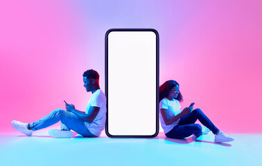 Poster - Cool mobile app. African American couple sitting near big smartphone with mockup, using modern gadgets, advertising new application or website, promoting your product or service in neon light