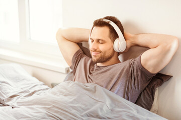 Aufkleber - Bedtime Relaxation. Smiling Man Enjoying Music In Earphones Relaxing Sitting In Bed At Home. Free Space