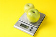 © New Africa - Electronic kitchen scale with apples on yellow background, closeup