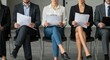 © velikiyzayats - A Diverse Group of Job Applicants Sitting in a Waiting Area for an Interview, Showcasing Different Ages, Genders, and Attire in a Modern Office Environment