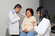 © Arlette - 80-year-old woman has her eyes, ears, and throat examined by a dark-skinned Latino doctor and his intern in the office as a checkup