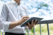 © Kawee - Close up of businessman using digital tablet while standing in park.