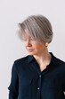 © Viktor Solomin/Stocksy - Mature woman with gray hair wearing a blue shirt and golden earrings
