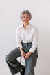 © Viktor Solomin/Stocksy - Portrait of a confident woman seated on a stool, wearing white shirt