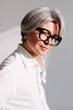 © Viktor Solomin/Stocksy - Stylish woman with gray hair and glasses posing confidently