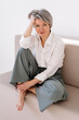 © Viktor Solomin/Stocksy - Mature woman in a stylish outfit poses gracefully on a sofa