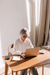 © Viktor Solomin/Stocksy - Senior woman working diligently on a laptop at a cozy wooden desk