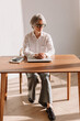 © Viktor Solomin/Stocksy - Older woman sitting at a wooden table in a bright office room