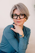 © Viktor Solomin/Stocksy - Stylish woman with short gray hair and glasses poses elegantly