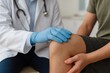 © Wararat - Knee Examination: A doctor in a medical coat, gently examines the knee of a patient during a physical examination, with medical equipment nearby, symbolizing healthcare and wellness.