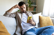 © Daniel - Bored man looking at phone at home sitting on the sofa.