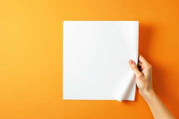 Poster - Blank white paper held by a hand on vibrant orange background.