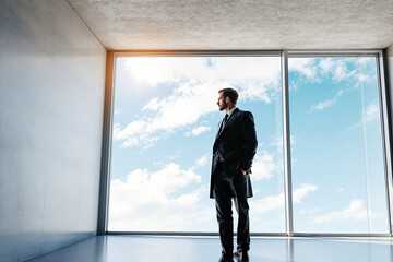 Poster - Businessman in suit standing in modern office with large window.
