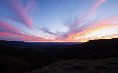 Poster - Dramatic sunset paints the sky with vibrant pink and orange hues over a dark, mountainous landscape. The horizon glows with the last light of day.