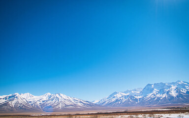 Poster - Snowy mountain range under a clear blue sky on a bright sunny day.  The landscape shows a vast expanse of nature with snow-covered peaks and a clear atmosphere.