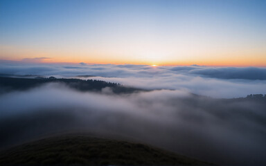 Aufkleber - Sunrise over a misty mountain range. Fog fills the valleys, with the sun breaking through clouds, coloring the sky in hues of orange and blue.
