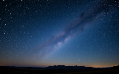 Poster - Vast night sky displays the milky way stretching across with countless stars. A dark horizon shows distant mountains in a serene, peaceful night scene.