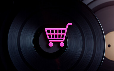 Aufkleber - Pink shopping cart icon placed on a black vinyl record, suggesting online music purchases or the concept of buying records digitally. The background is dark and out of focus.