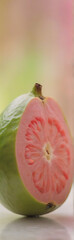 Aufkleber - A halved guava fruit reveals its vibrant pink flesh and seeds, sitting beside a whole fruit with green skin. The background is softly blurred in pastel shades.