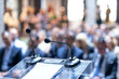 © wellphoto - Microphones in focus, unrecognizable people in background at business conference, corporate presentation, workshop, coaching training, news conference, company meeting, public or political event