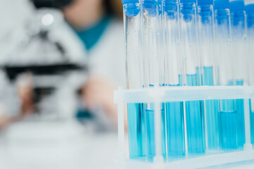 Poster - A closeup shot of a rack filled with test tubes containing blue liquid, highlighting the precision and focus of laboratory experiments. blurred background suggests scientist working with a microscope
