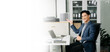 © Nuttapong punna - Confident businessman in suit, working on laptop and smartphone at office desk.