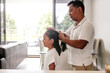 © Austockphoto - Asian father combing and tying daughter's hair inside home.