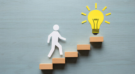 Poster - Paper Cutout Person Ascending Wooden Blocks Towards a Light Bulb on Grey Backdrop