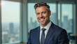© f_bossa - A portrait headshot photo of a friendly professional CEO executive business worker: A smiling, mature businessman with graying hair stands confidently in a modern office, overlooking a cityscape