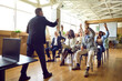 © Studio Romantic - Diverse active audience asking questions at business training meeting with coach. Group of young and mature multiethnic people sitting in rows in office, smiling and raising their hands up