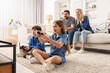 © New Africa - Cute kids playing video games while their parents resting on sofa indoors