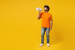 © ViDi Studio - Full body young surprised excited shocked Indian man wear orange t-shirt casual clothes hold megaphone scream announces discounts sale Hurry up isolated on plain yellow background. Lifestyle concept.