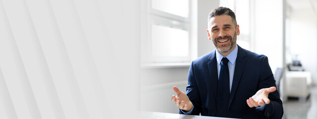 Aufkleber - A middle aged businessman in a suit holds a discussion in a well-lit office. He appears confident and approachable, showcasing a successful and professional lifestyle in a contemporary environment.