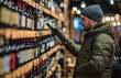 © Ahsan - Man shopping for wine at liquor store choosing bottle from shelf beverage alcohol selection in market aisle