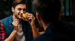 © Postmodern Studio - Young caucasian male enjoying a burger in a cozy restaurant setting